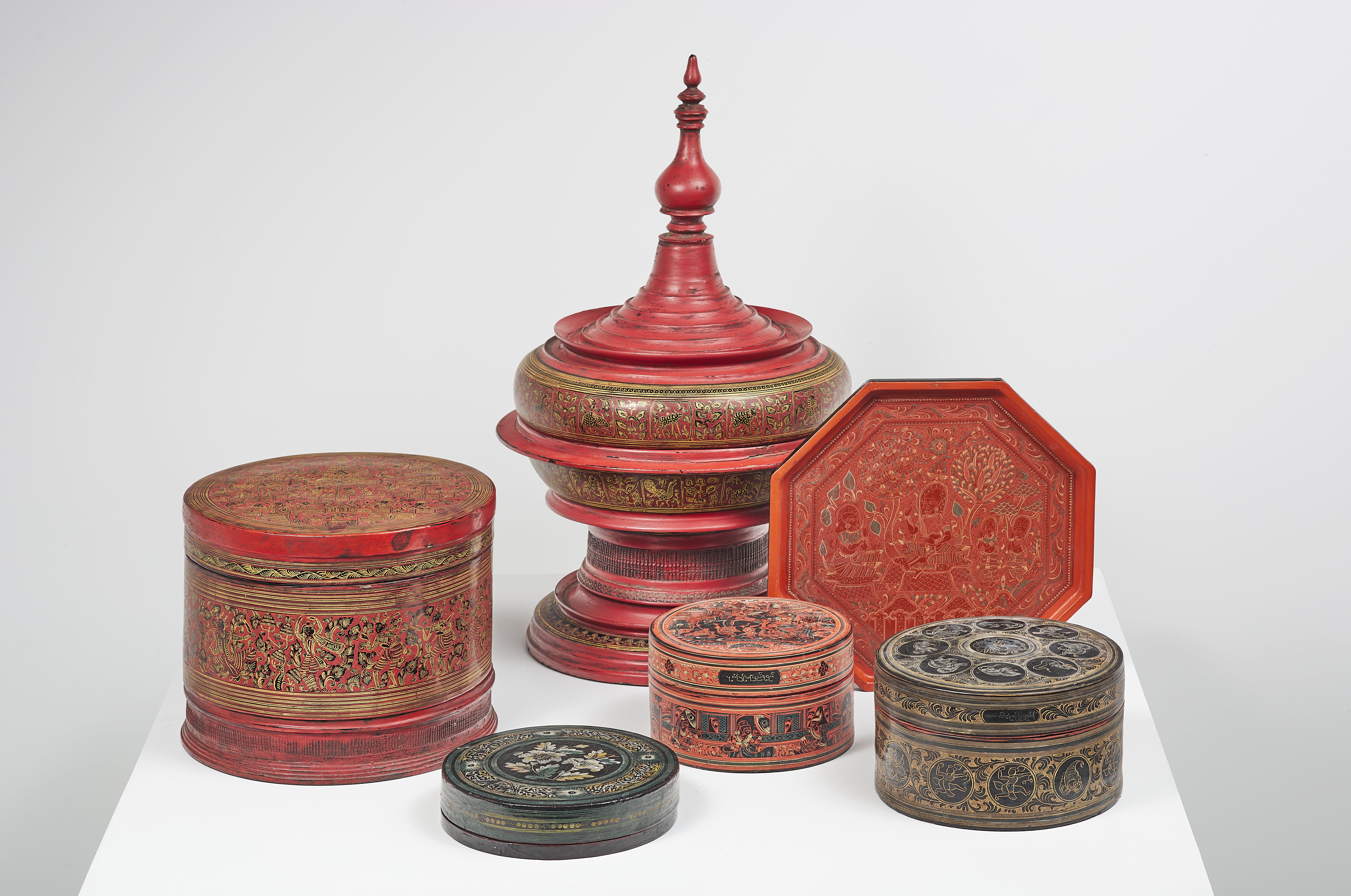 Burma late 19th-20th century Set of five covered boxes and a tray in red and black lacquered wood, including a large Hsun-ok offering box with gilded decoration of birds and foliage, the lid taking the shape of a stupa, four circular betel boxes and an octagonal tray decorated with scenes of characters, animals of the zodiac, flowers...