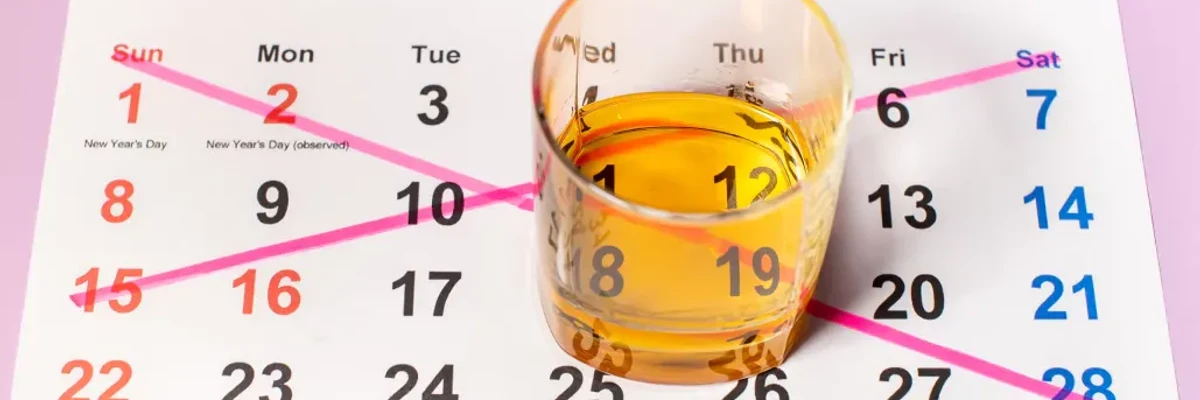 Verre de whisky posé sur un calendrier avec des dates marquées en rose.