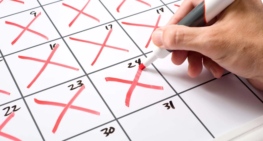 Main qui marque un jour sur un calendrier avec des croix rouges.