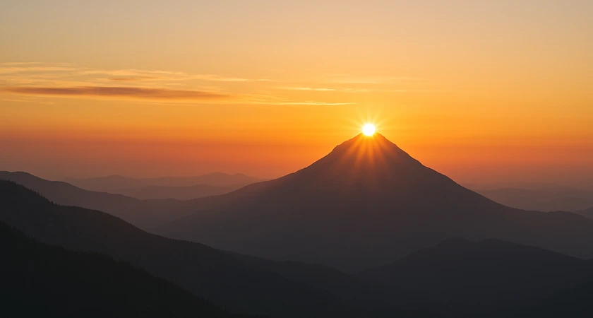 Coucher de soleil illuminant le sommet d'une montagne avec un ciel orangé en arrière-plan.