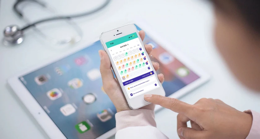 Personne utilisant une application de suivi de santé sur un smartphone avec une tablette en arrière-plan.
