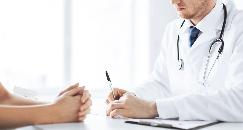 Consultation médicale entre un médecin en blouse blanche et un patient assis à un bureau.