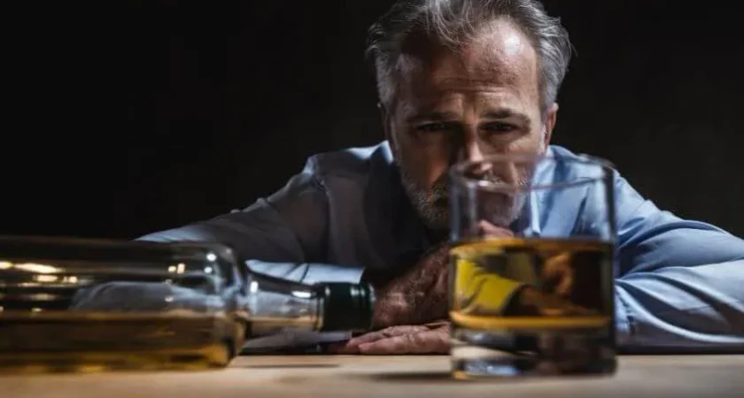 Homme pensif avec un verre de whisky sur une table en bois.
