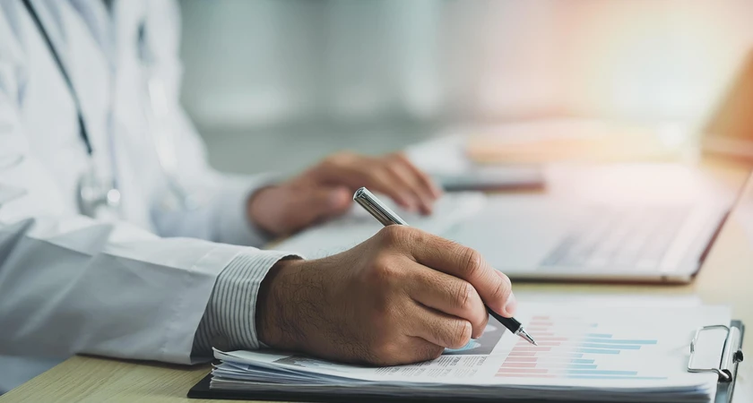 Médecin examinant des graphiques et prenant des notes sur un bureau.
