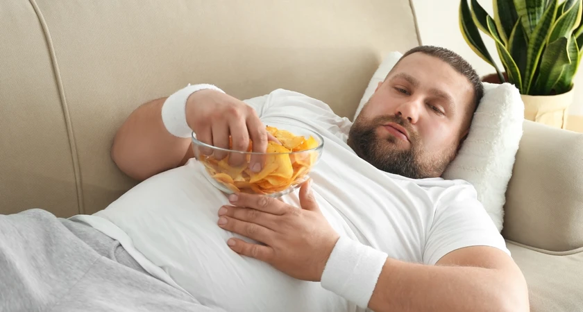 Homme allongé sur un canapé mangeant des chips d'un bol.