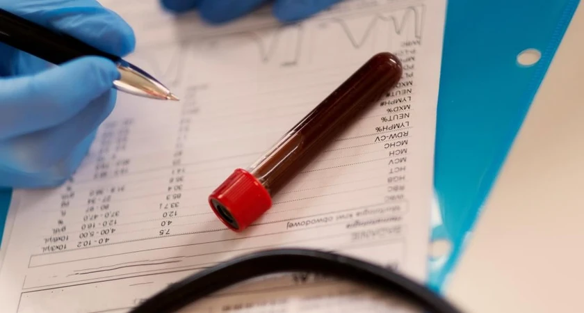 Tube de prélèvement sanguin posé sur un document avec des résultats de test, main gantée tenant un stylo.
