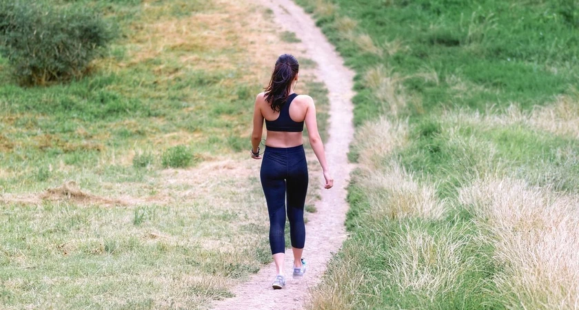 Femme marchant sur un sentier dans la nature, portant une tenue de sport.
