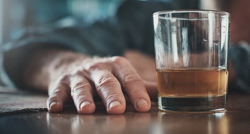 Main posée à côté d'un verre de whisky sur une table en bois.