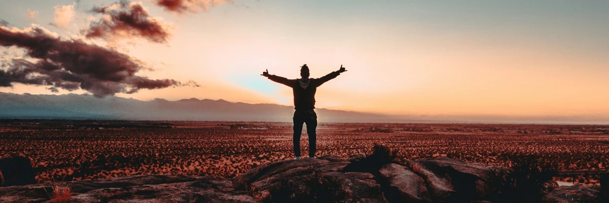 Personne levant les bras au coucher du soleil sur un paysage désertique.