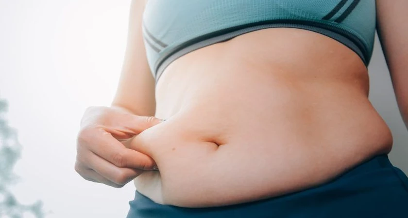 Personne tenant la peau de son ventre, mise en valeur de la graisse abdominale.