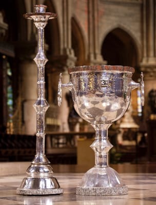 Gros plan sur le chandelier Pascal et la cuve baptismale argentés et miroitants