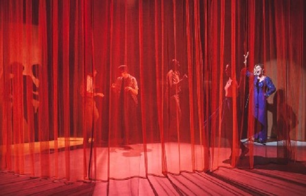acteurs sur scène derrière un rideau rouge transparent