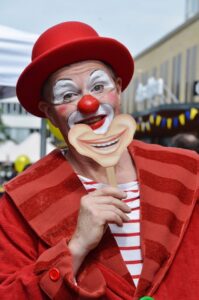 Clown grimé avec un masque qui représente une boucje qui rit.