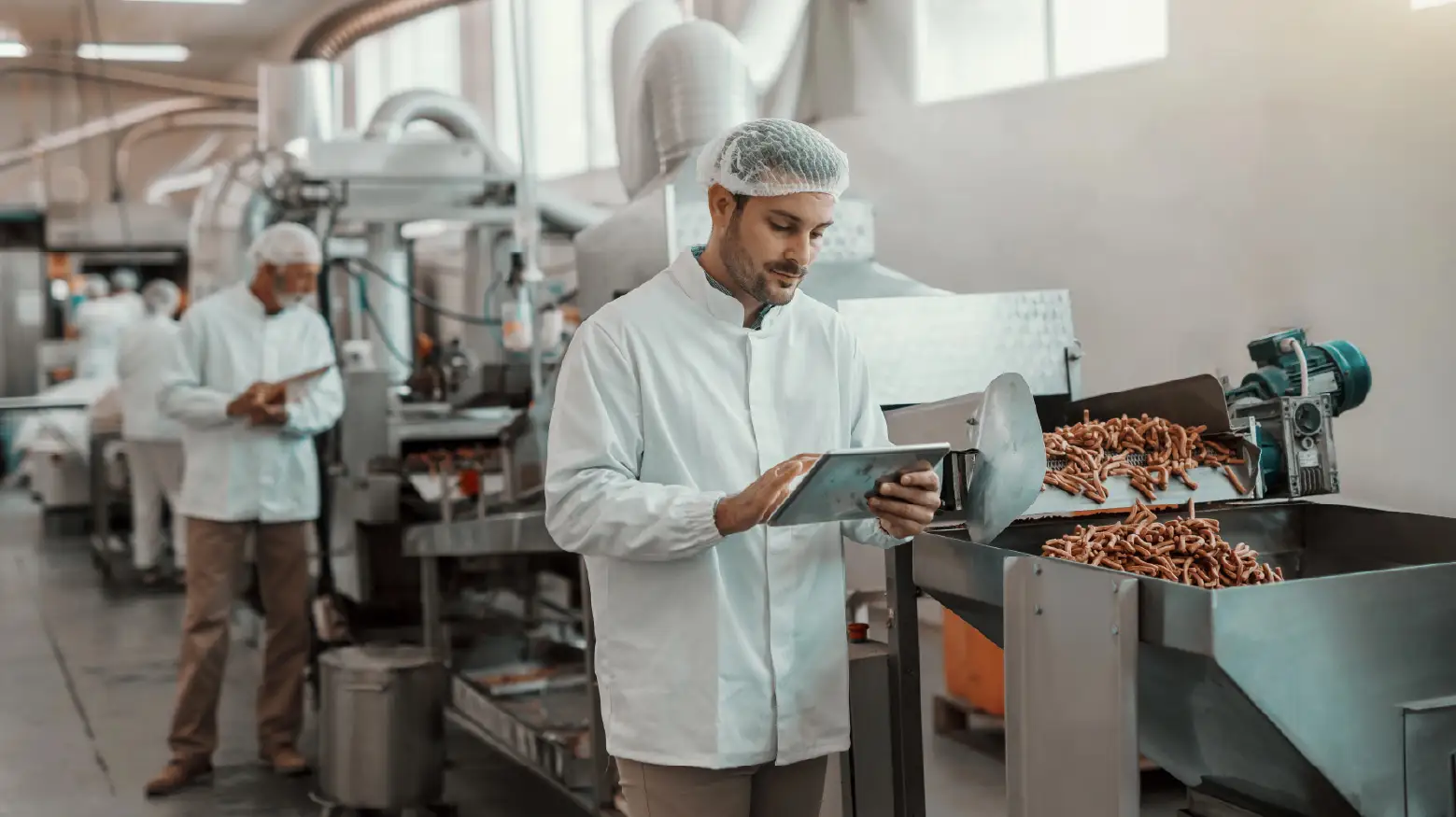 Young Caucasian serious supervisor evaluating quality of food in food plant while holding tablet.