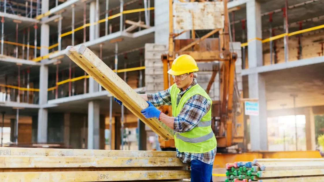 Un travailleur de la construction transfère une livraison de poutres de construction.