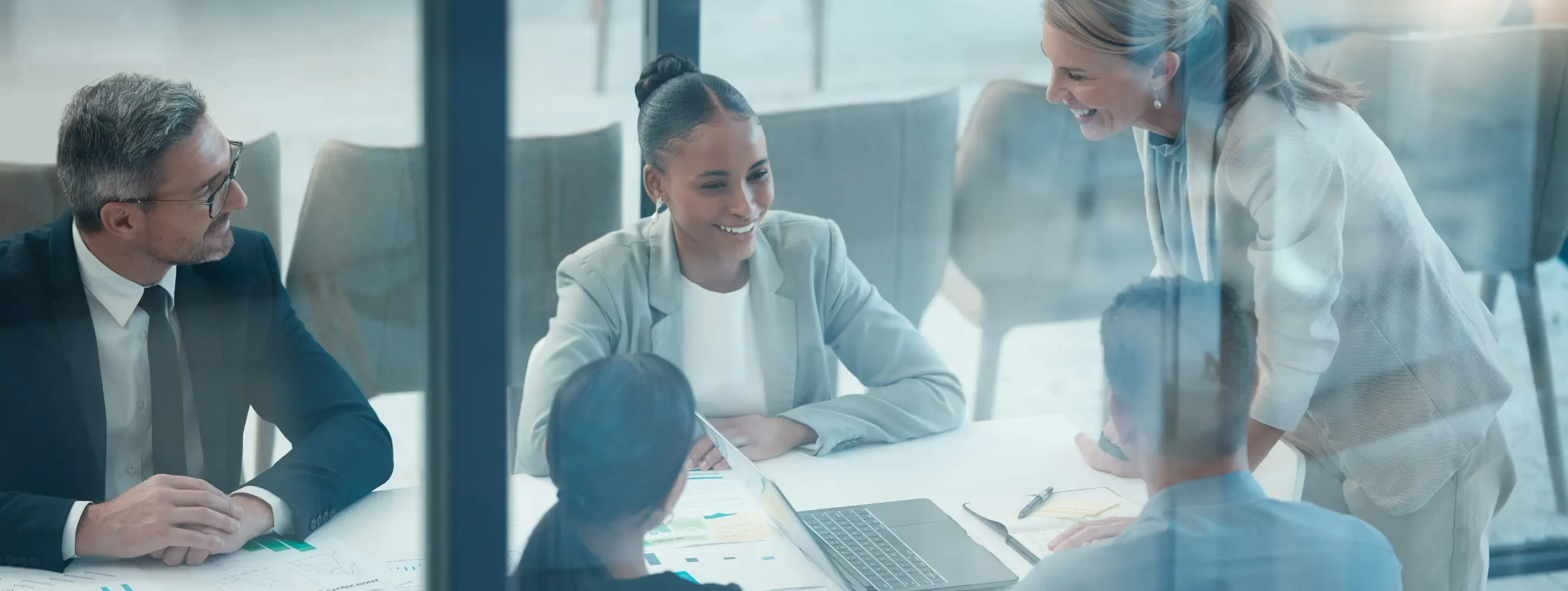 A diverse group in an office gathers around a table and discuss a project enthusiastically