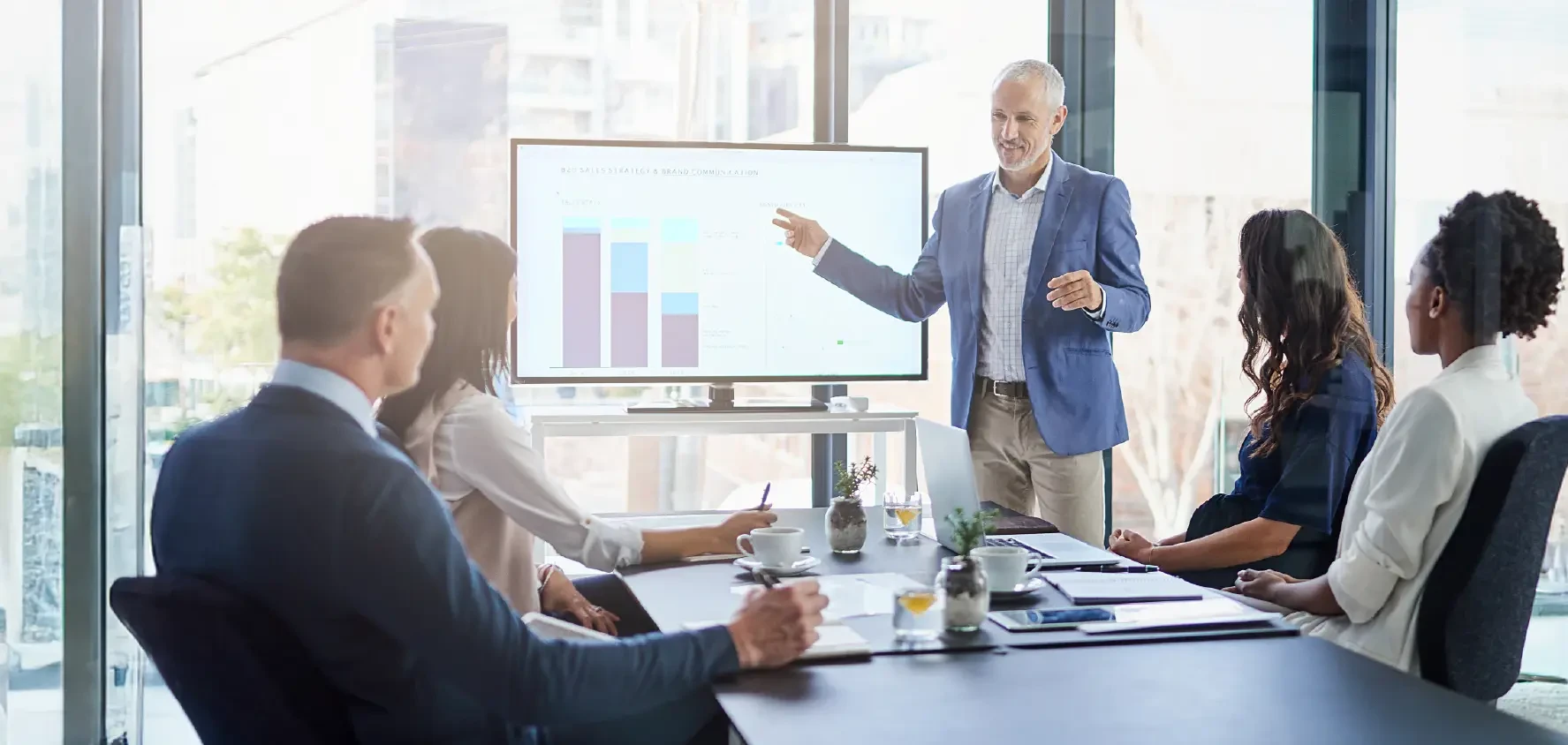 A man is showing some information on a monitor to the attendees in a meeting