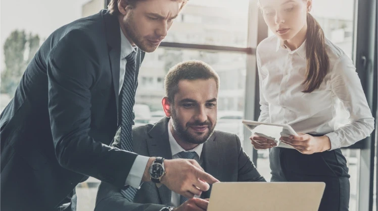 Two men and a woman in an office look attentively at some information on a laptop
