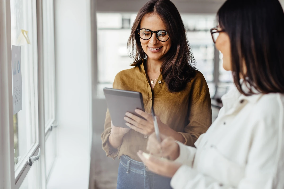 Femme souriant et regardant un écran de tablette avec une collègue à ses côtés
