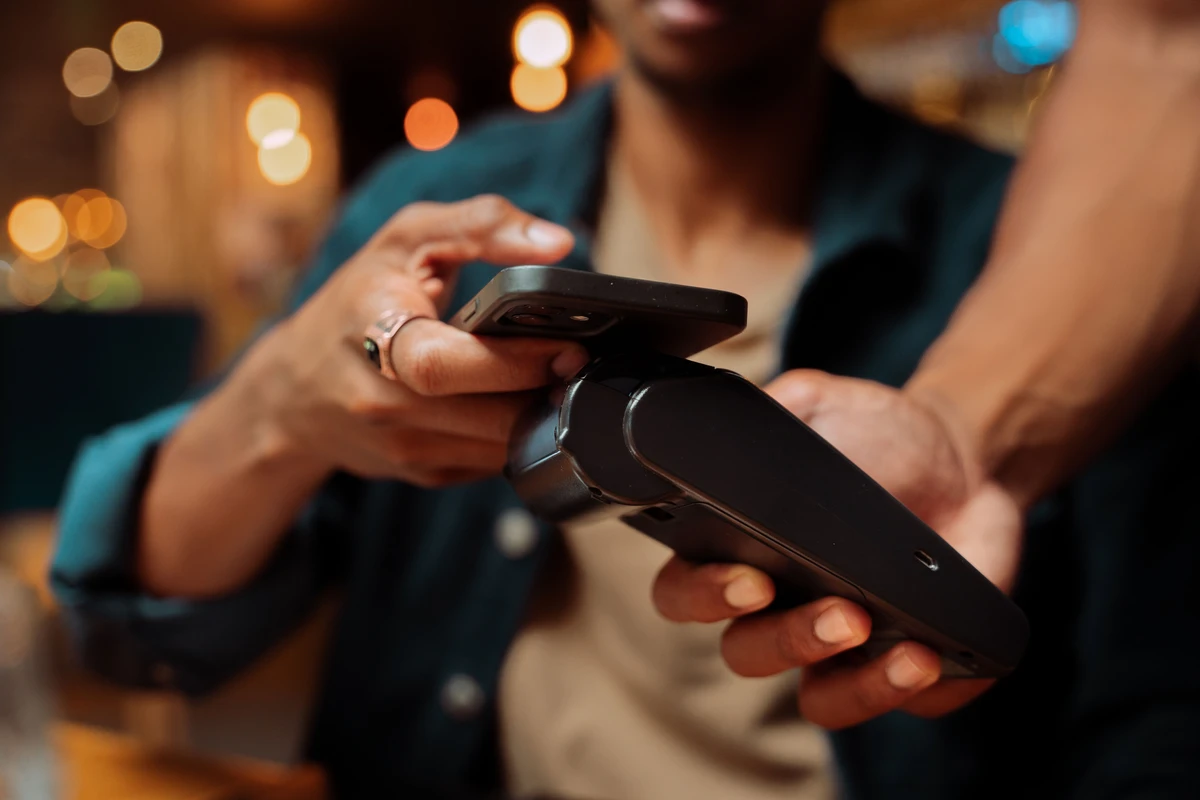 Close up of customer paying card machine with with mobile device