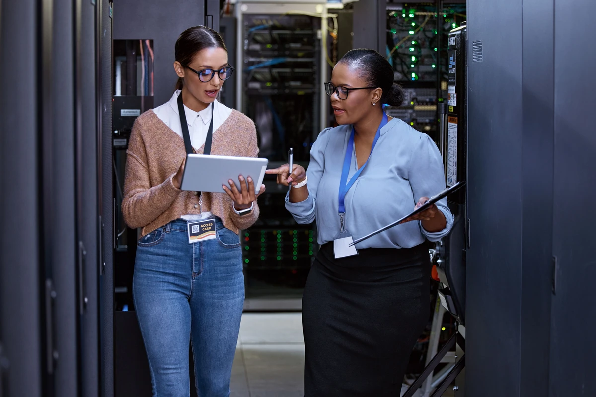 Female colleagues talking, server room with a tablet for cyber security