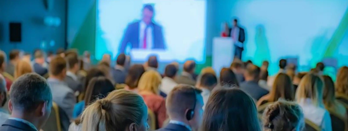 Salle de conférence avec un orateur en train de parler, tandis que des participants écoutent attentivement.