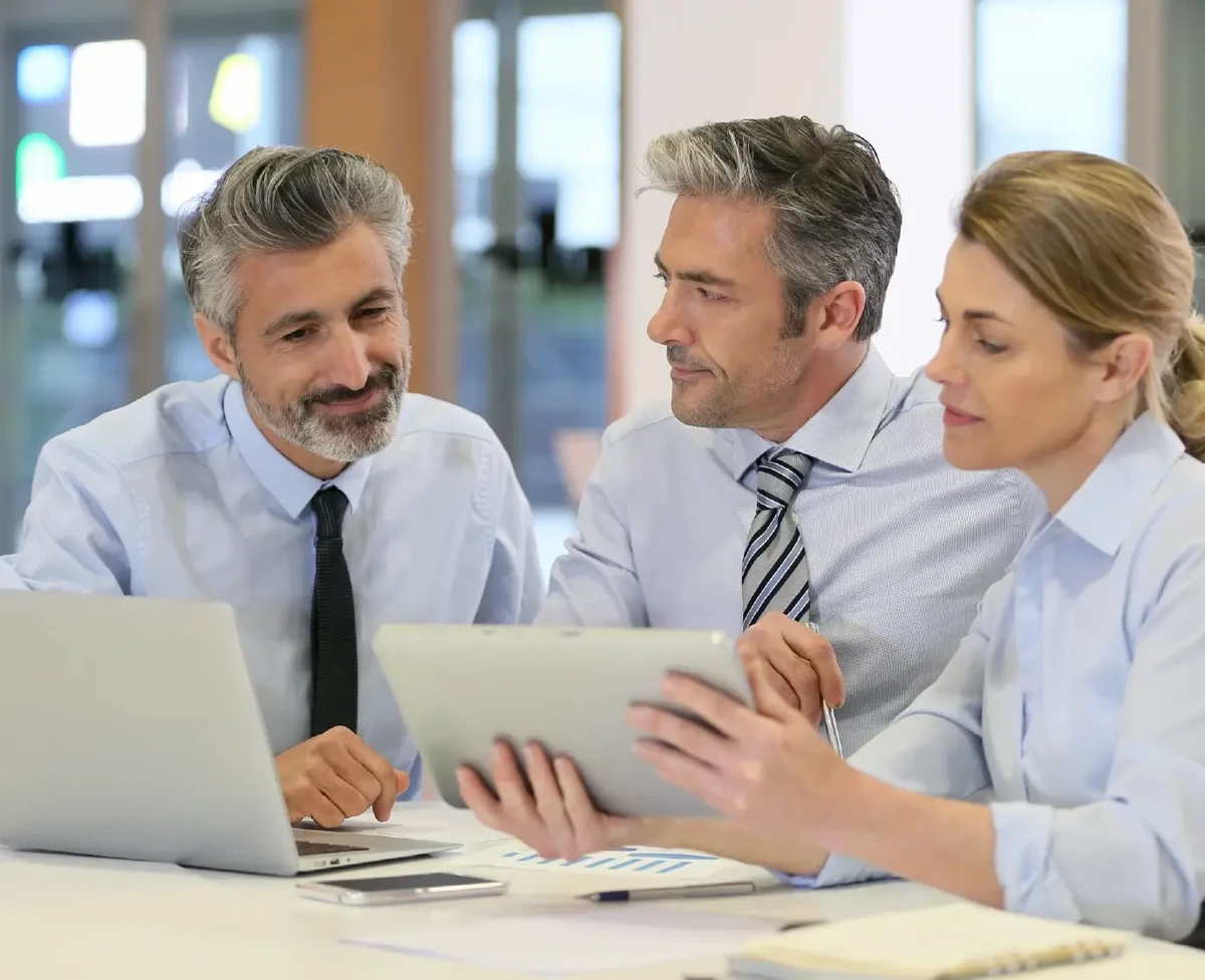 Three professional people working with SAP Analytics Cloud, analyzing data in office with computer and tablet.