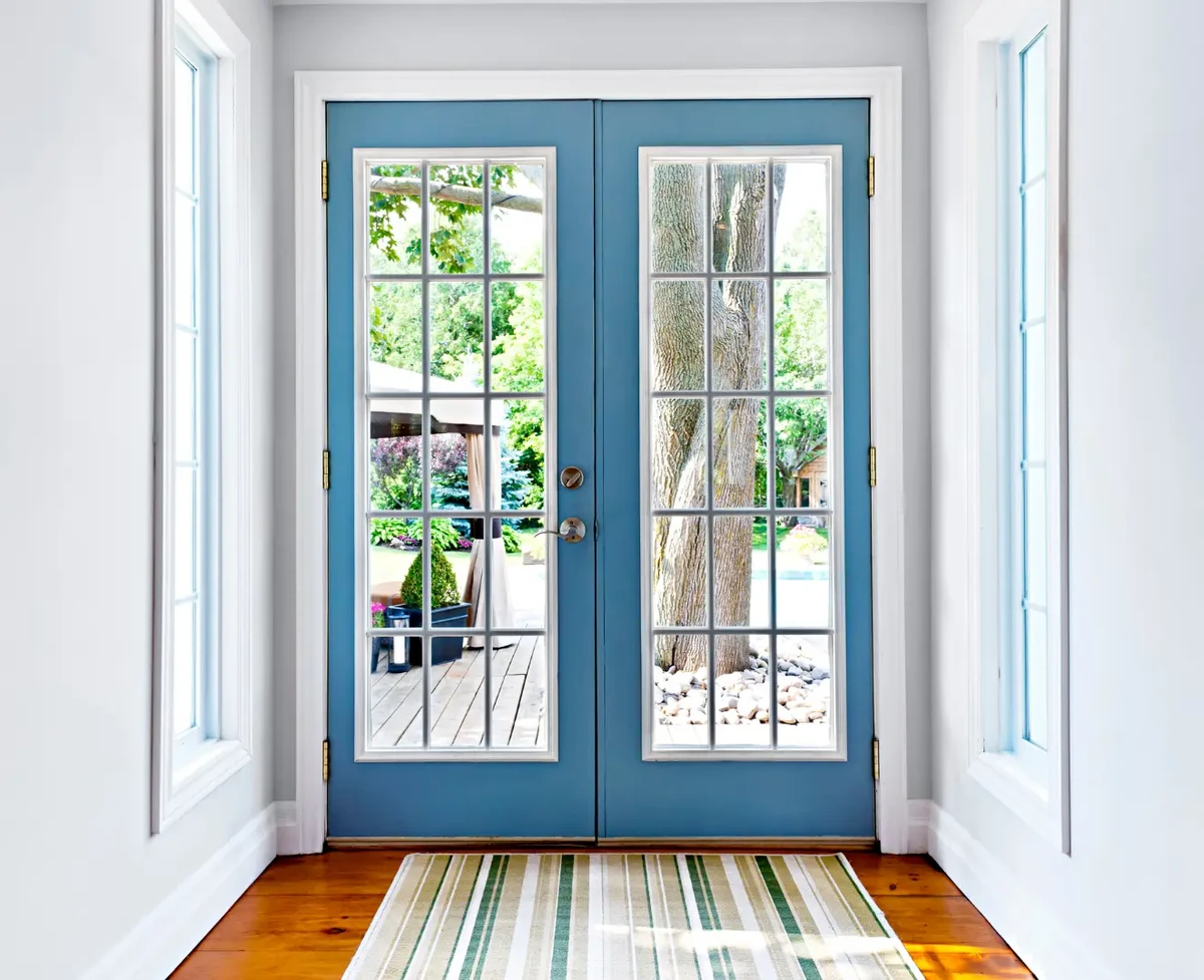A glass door with blue hinges overlooding a vinrant garden