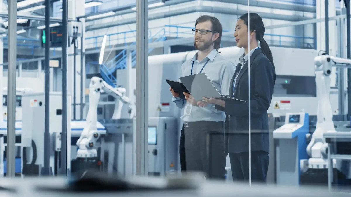 Male Technician and Female Businesswoman Standing in Office, Talking, Using Computers and Monitoring Production at a Modern Automated Electronics