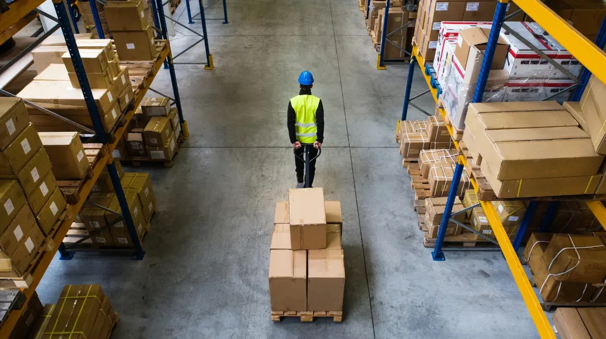 Un employé d’entrepôt déplace des boîtes dans un grand entrepôt aux étagères remplies.