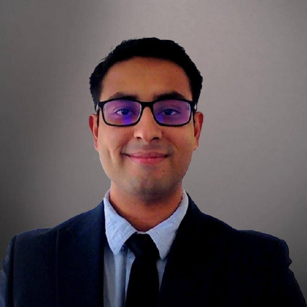 A smartly dressed businessman with black hair and wearing tinted glasses smiling at the camera