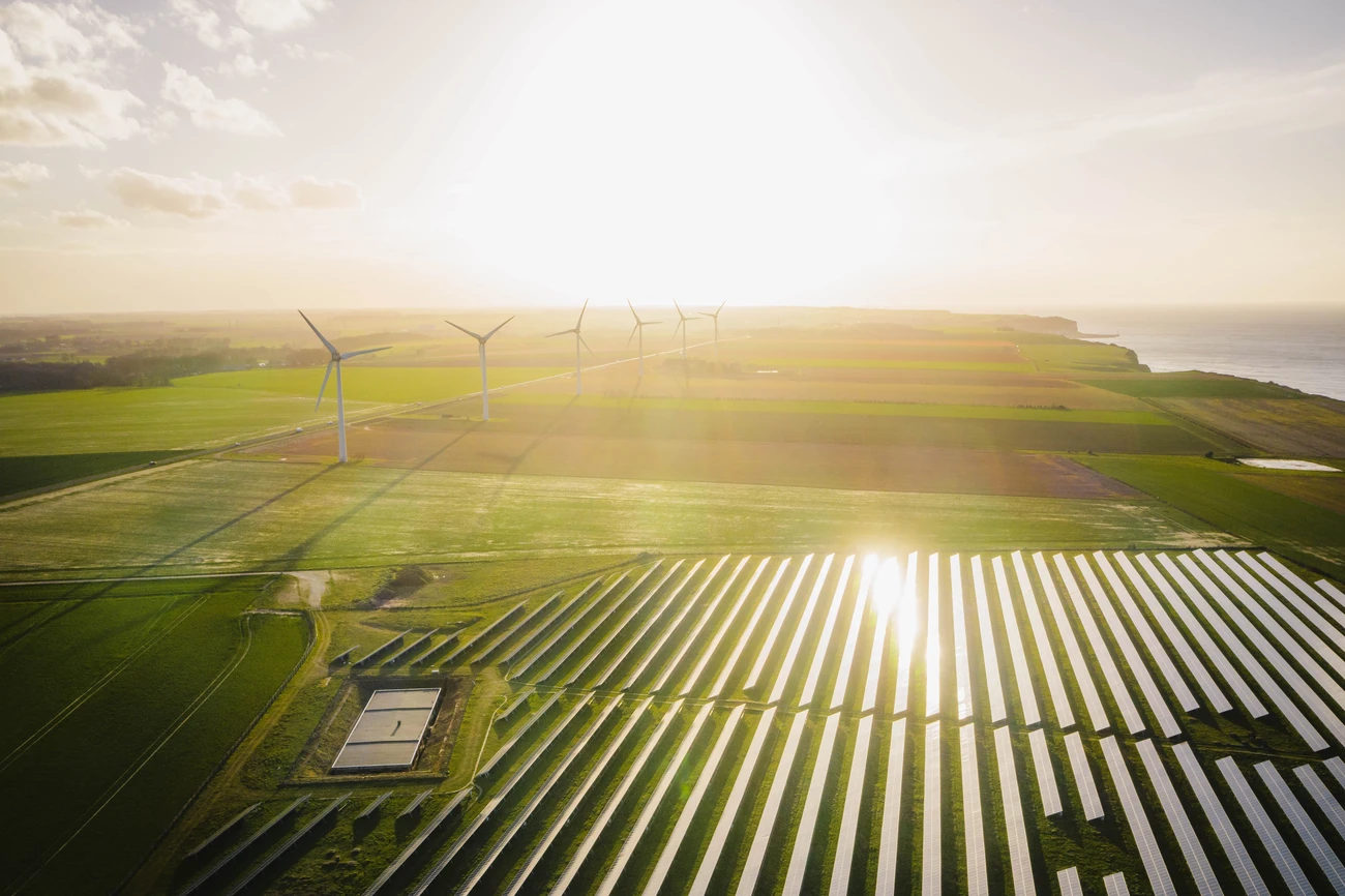 Windmills and solar panels farm in green fields close to the ocean.