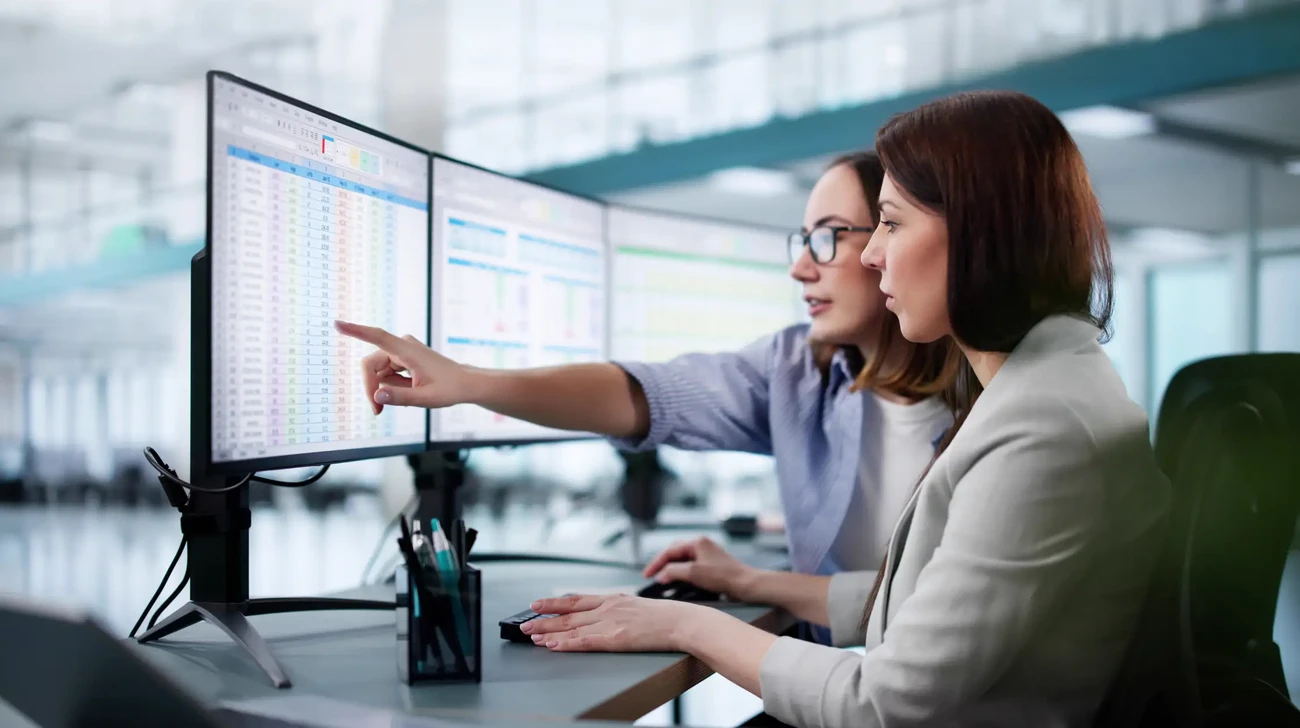 Two women at an office are looking at some financial data on a computer attentively