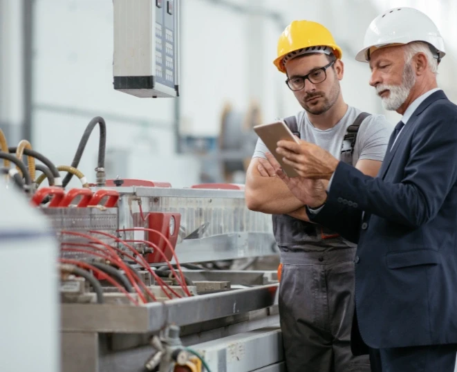 A manager and a factory worker are looking at the manufacturing data on a laptop