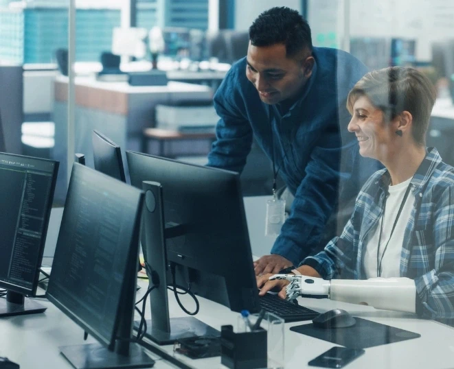 eamwork In Diverse Inclusive Office: Project Manager Talks with Woman with Disability with Prosthetic Arm Work on Desktop Computer