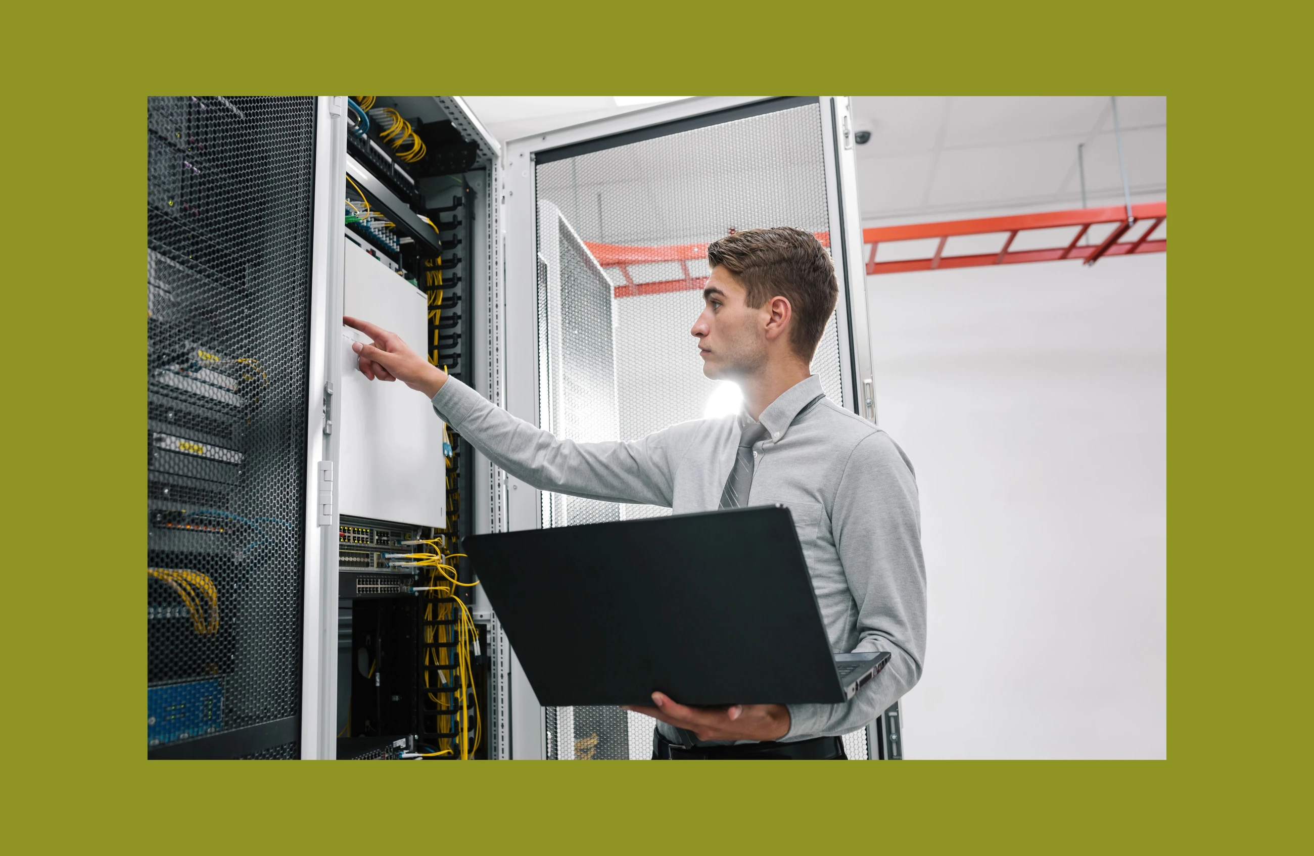 A man in a data center checks the information on a laptop and matches it wit h a list attached to a wall