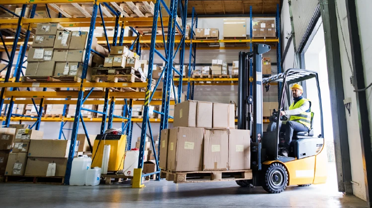 Homme dans un entrepôt transportant un chariot avec des boîtes pour la distribution.