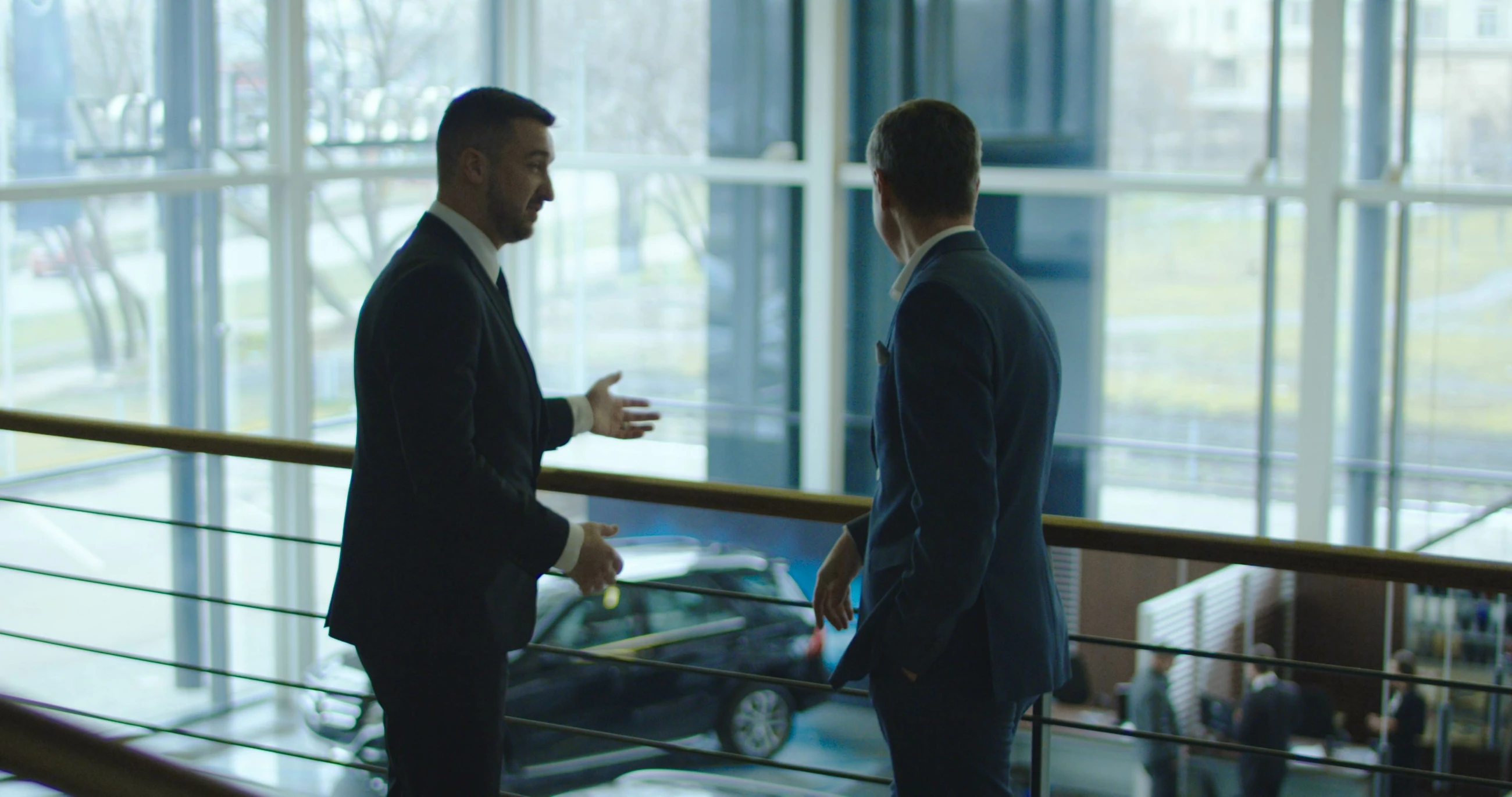 Two men having conversation on balcony in car showroom.