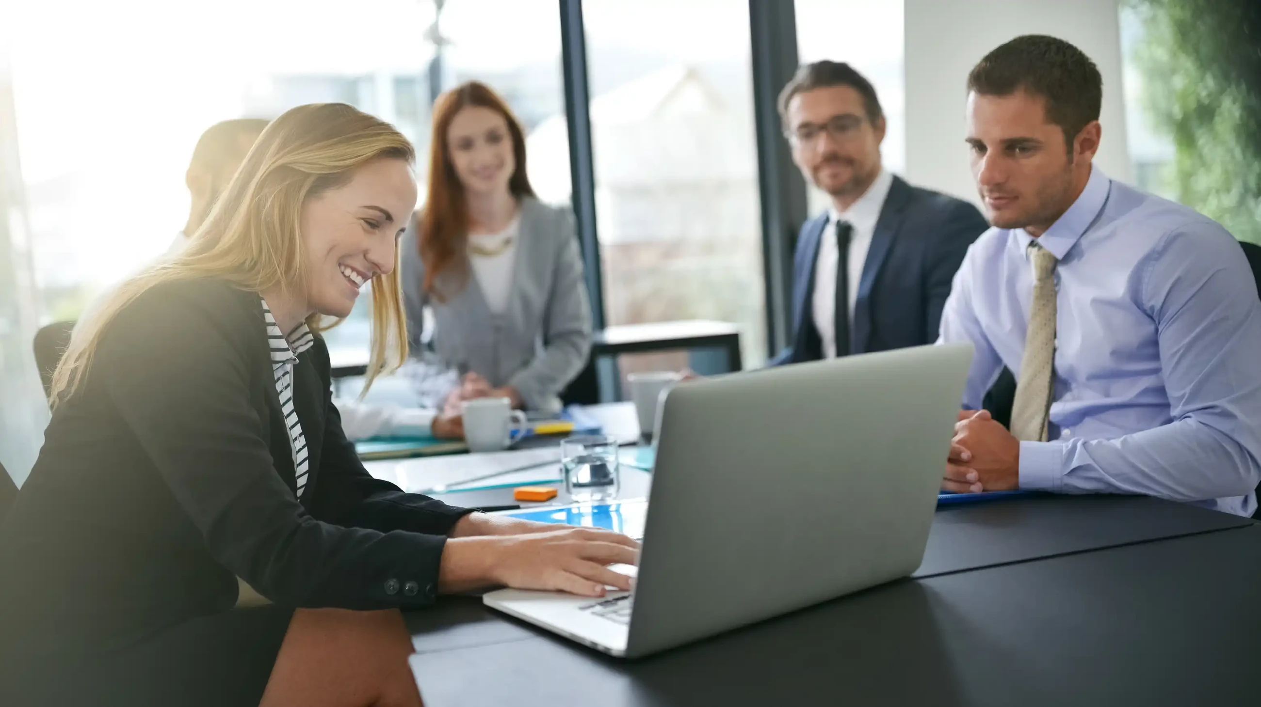 Office with professional colleagues and a woman demonstrating SAP business intelligence solutions on her computer.