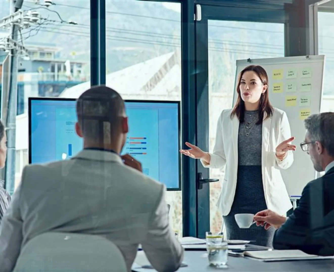 Une femme dans un bureau explique des données et une infographie sur un tableau à une équipe dynamique.
