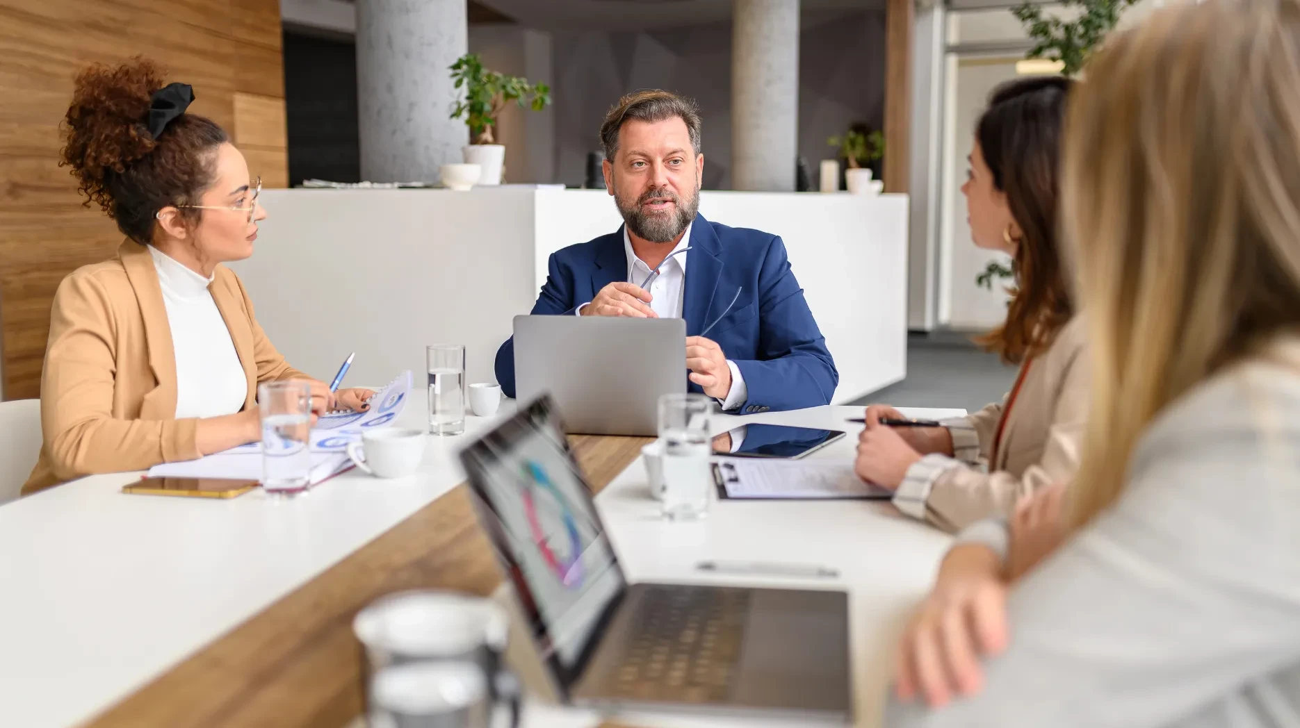 A team in an office gathers around a table and go through some business data on their computers