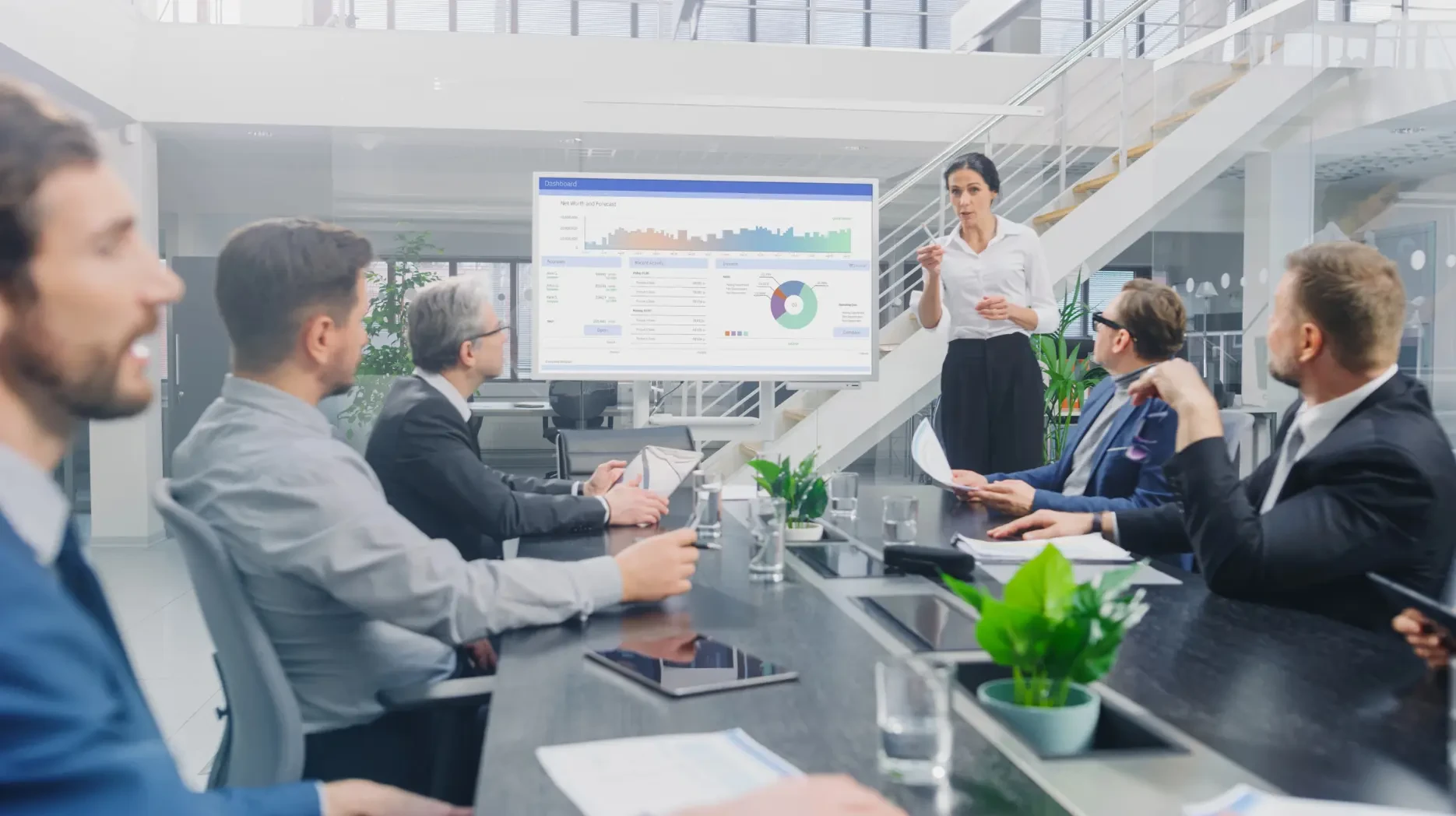 A dynamic team gathered around a meeting table, where a woman is explaining some information and infographs on a board to the team members