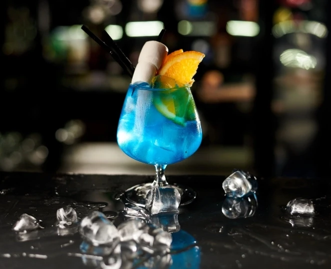 A picture of a stricking blue cocktail with the blury background of a bar
