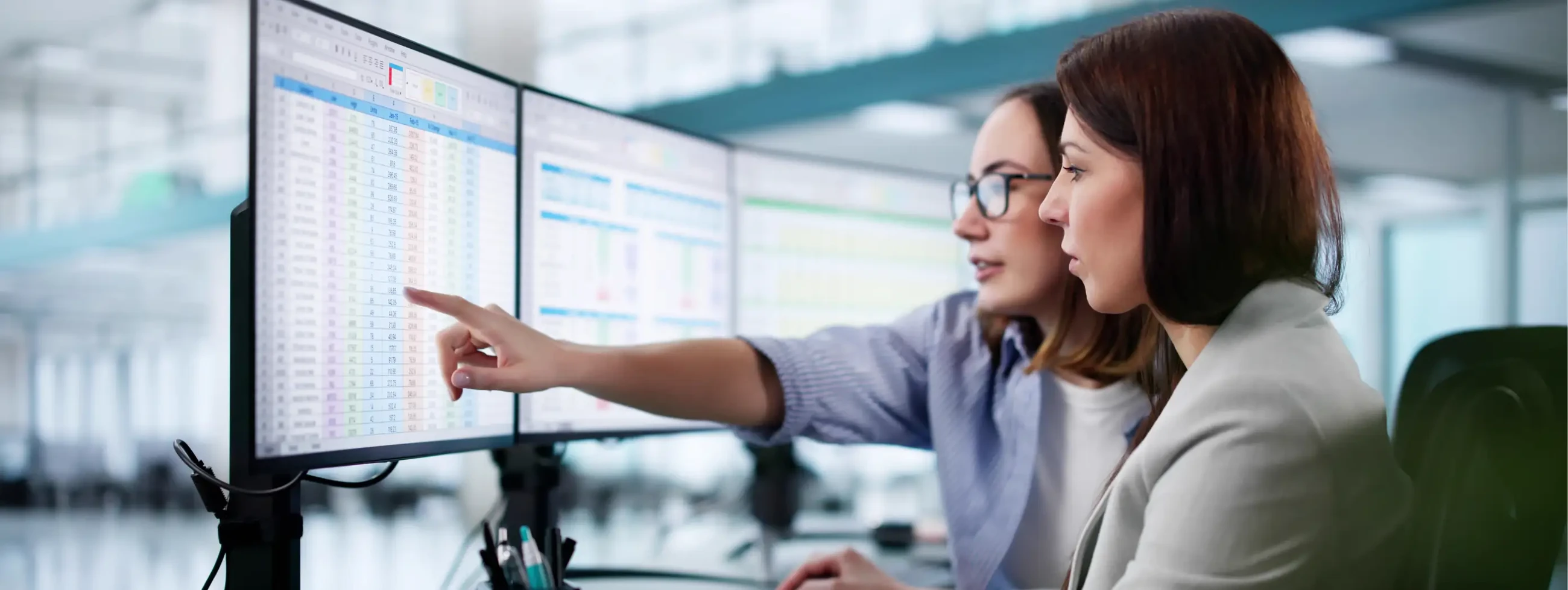 Two women at an office are looking at some financial data on a computer attentively