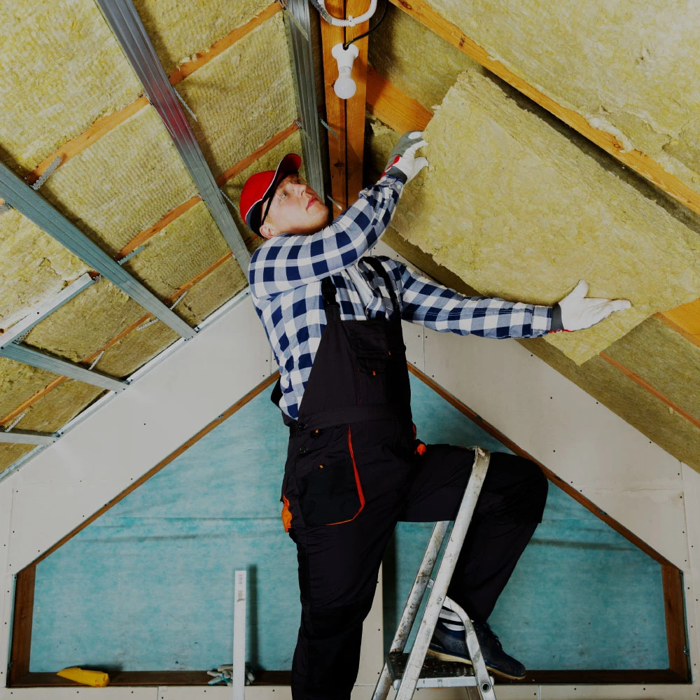 A workman fitting insulation into the roof of a building.