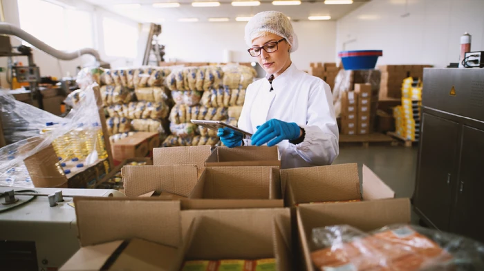 Female worker, packing food and beverage merchandise into boxes. She is on the ipad optimizing for cpg.