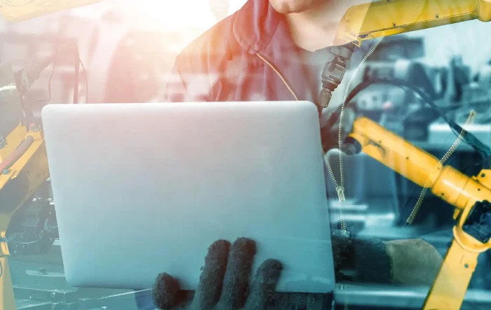 Un homme consulte des solutions pour améliorer la productivité sur son ordinateur portable, avec en arrière-plan une superposition d’images de machinerie industrielle.