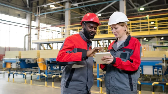 Two workers in a manufacturing factory looking at a tablet to follow up on a project