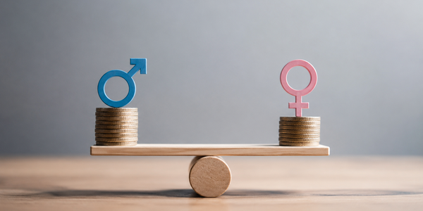 Die Abbildung zeigt eine Wippe mit zwei Stapeln Münzen, auf denen Symbole für Geschlechter platziert sind: ein blaues Männer-Symbol a.d. linken Seite und ein rosa Frauen-Symbol auf der rechten Seite. Das Bild thematisiert die Gleichheit der Geschlechter.