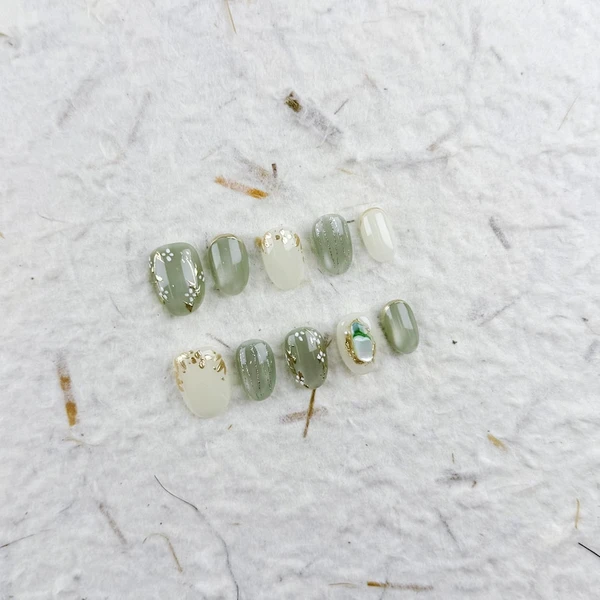 Ongles courts ovales frais à presser en vert pâle et blanc avec des fleurs blanches, des touches dorées et une finition brillante, parfaits pour les